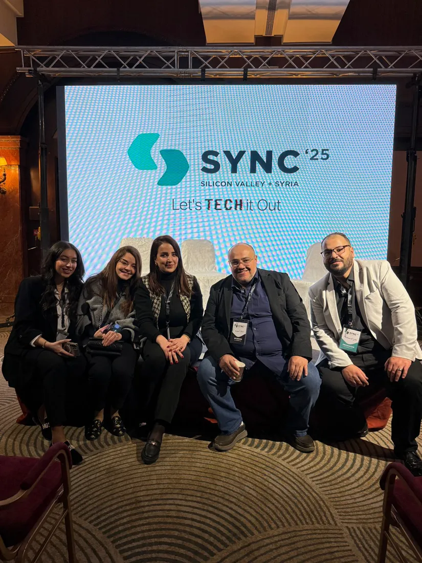 The team seated in front of the SYNC '25 stage screen